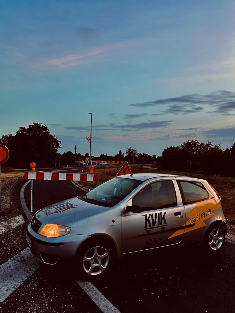 White hatchback car with orange accents parked at construction site barrier during twilight