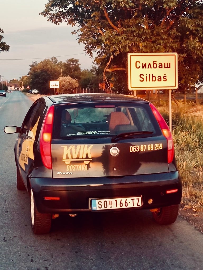 Taxi car parked on road next to Silbas town sign with golden hour sunlight and trees