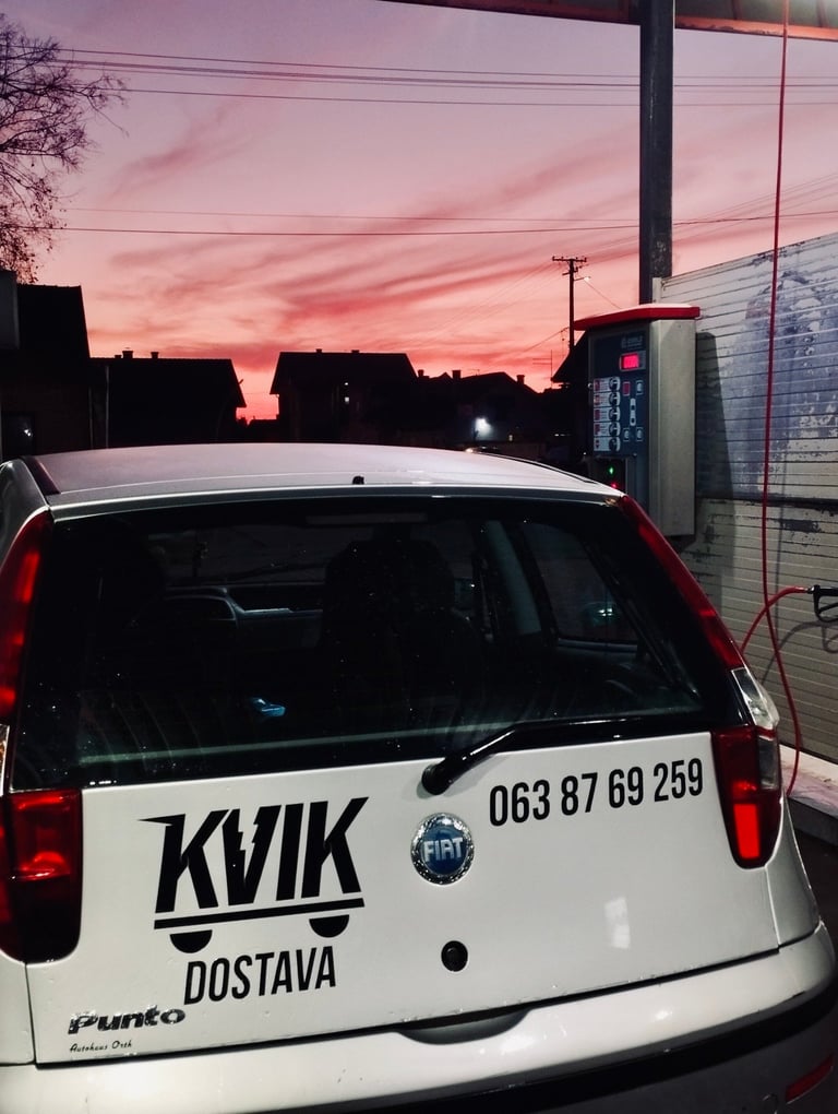 White Fiat delivery vehicle with KVIK DOSTAVA branding parked at sunset with pink sky and utility poles in background
