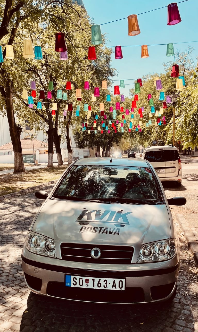 A silver taxi car parked under colorful hanging lanterns on a tree-lined street