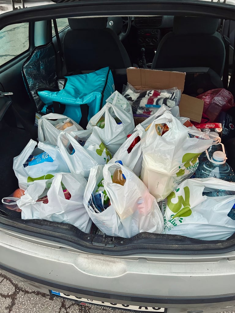 Car trunk filled with multiple white plastic shopping bags and cardboard boxes containing groceries and household items